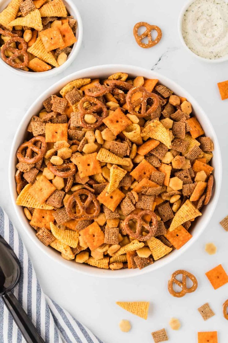 two bowls filled with cheetos and pretzels next to some crackers