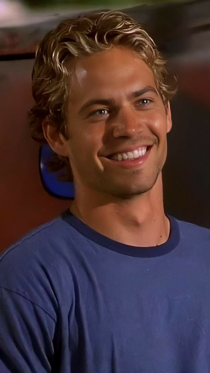 a young man with curly hair smiling at the camera while wearing a blue t - shirt