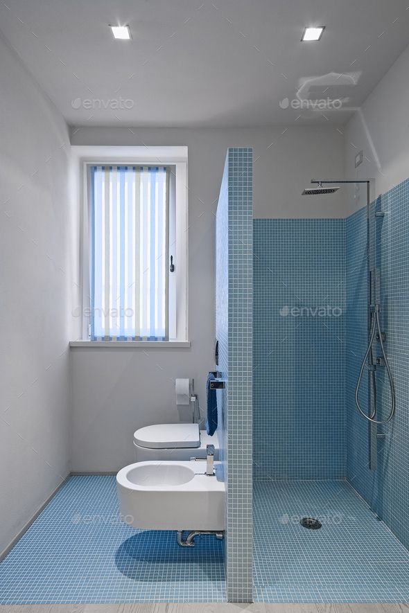 a blue tiled bathroom with a white toilet and bidet in the shower stall area