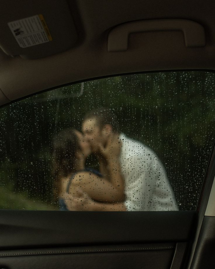 a man and woman kissing in the back seat of a car on a rainy day