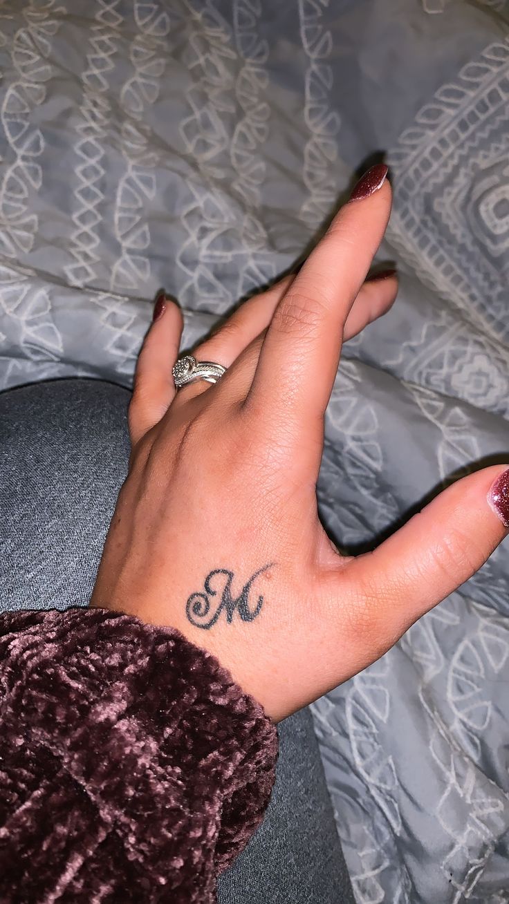 a woman's hand with a ring on it and the letter m tattooed on her thumb