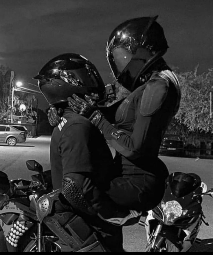 black and white photograph of two people sitting on a motorcycle with their helmets on,