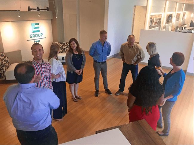 a group of people standing in a room talking to each other and smiling at the camera