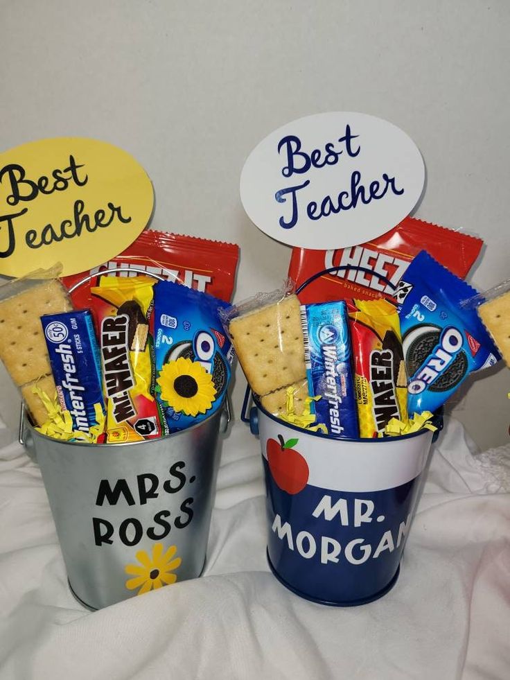 two buckets filled with different types of candy and crackers on top of a bed