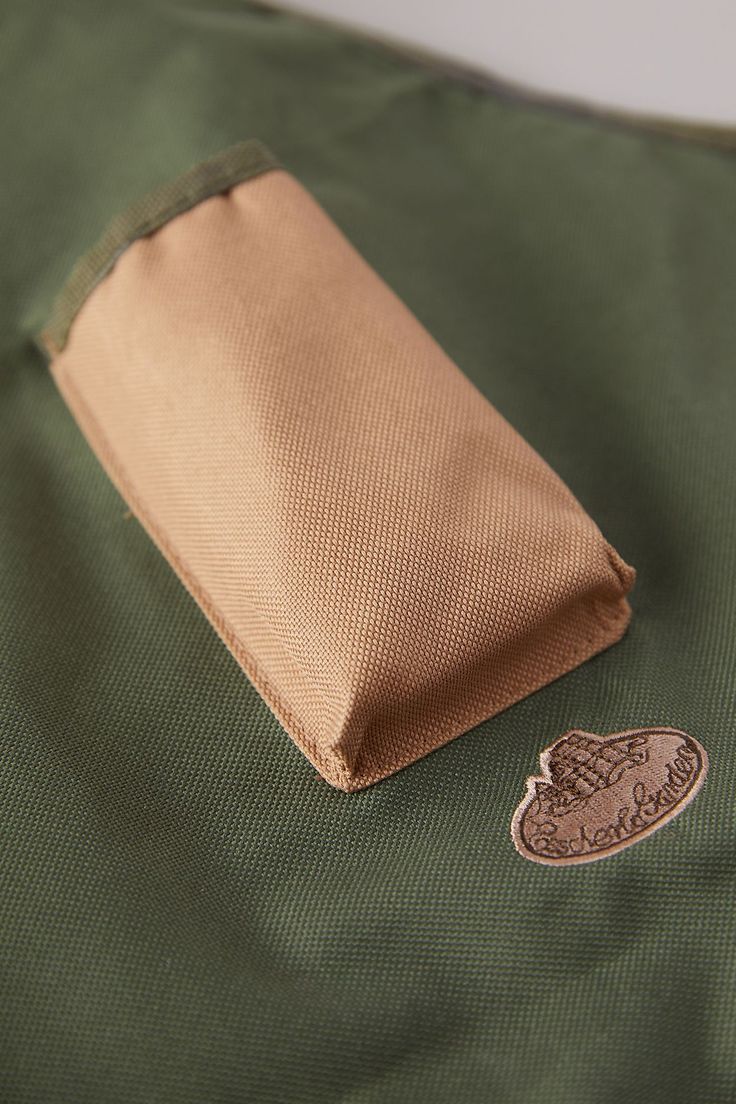 a green jacket with a brown heart patch on the side and a tan zippered pouch attached to it