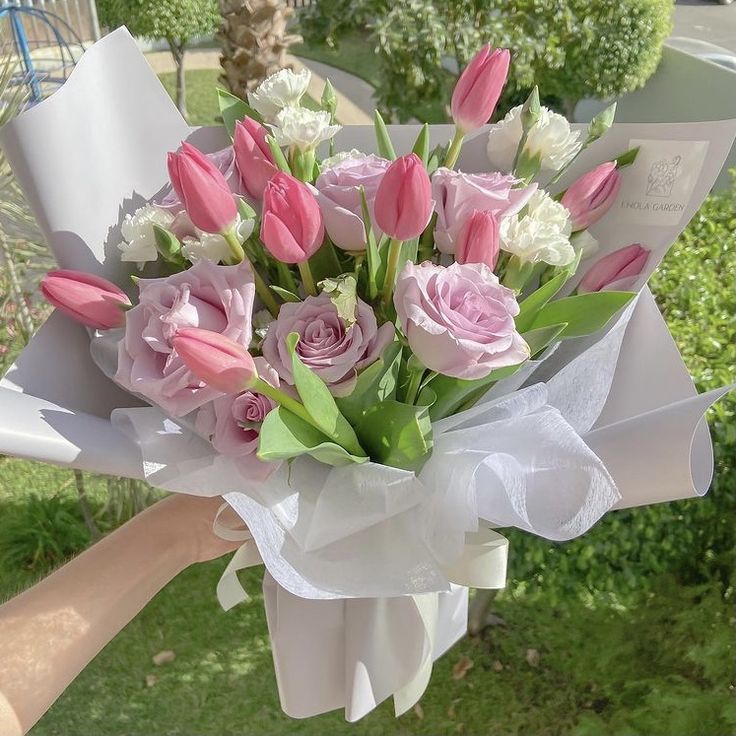 a bouquet of pink and white flowers is held by someone's hand in the park