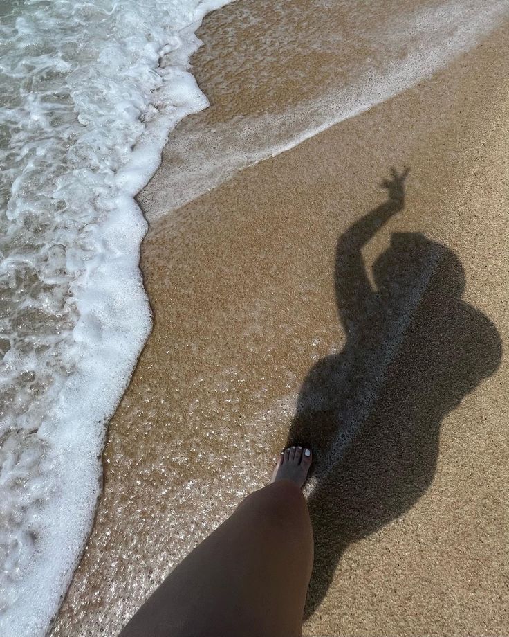 a person standing on the beach with their shadow in the sand and water behind them