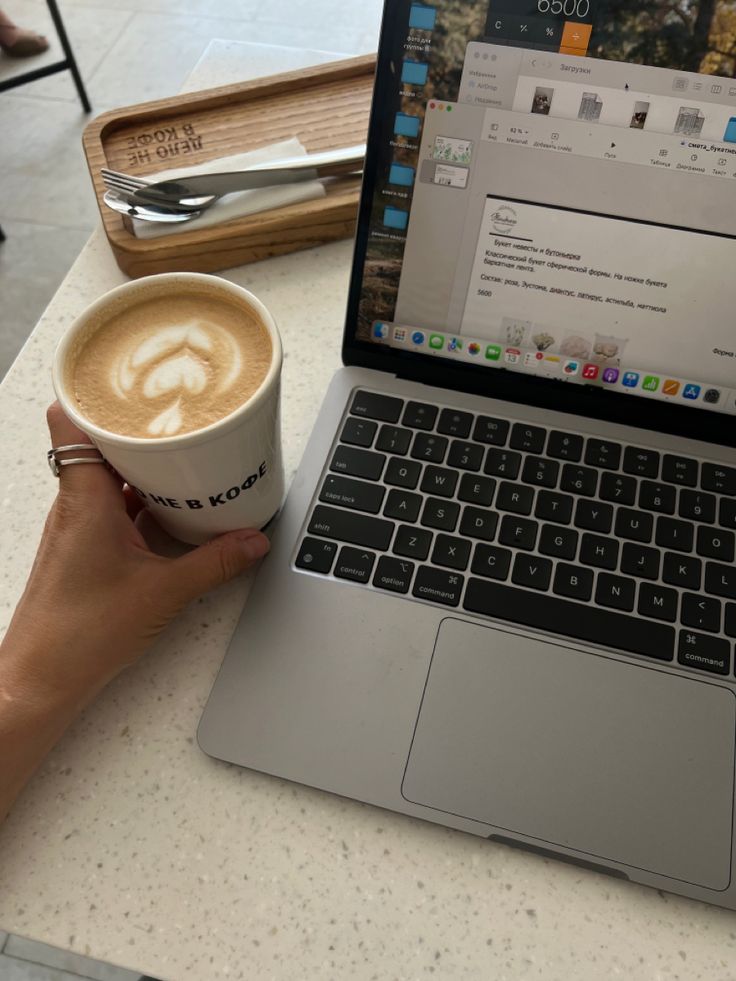 a person holding a cup of coffee in front of a laptop computer on a table