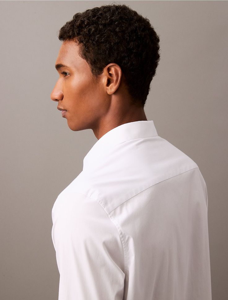 a young man in a white shirt looking off to the side with his right hand on his hip