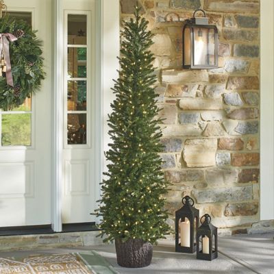 a christmas tree sitting on the front porch next to a lantern and lanterns with wreaths