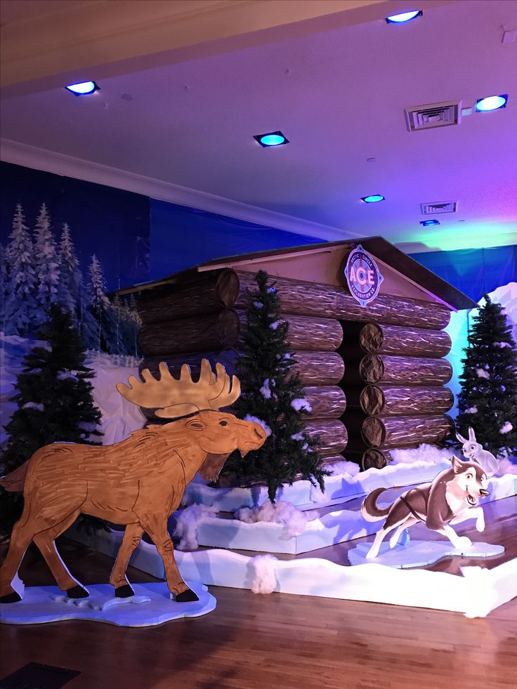 an indoor winter scene with fake moose, log cabin and reindeer running through the snow