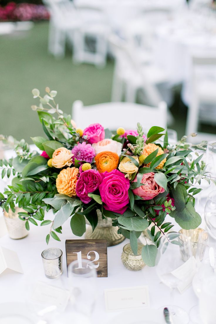 an arrangement of colorful flowers and greenery on a table at a wedding or reception