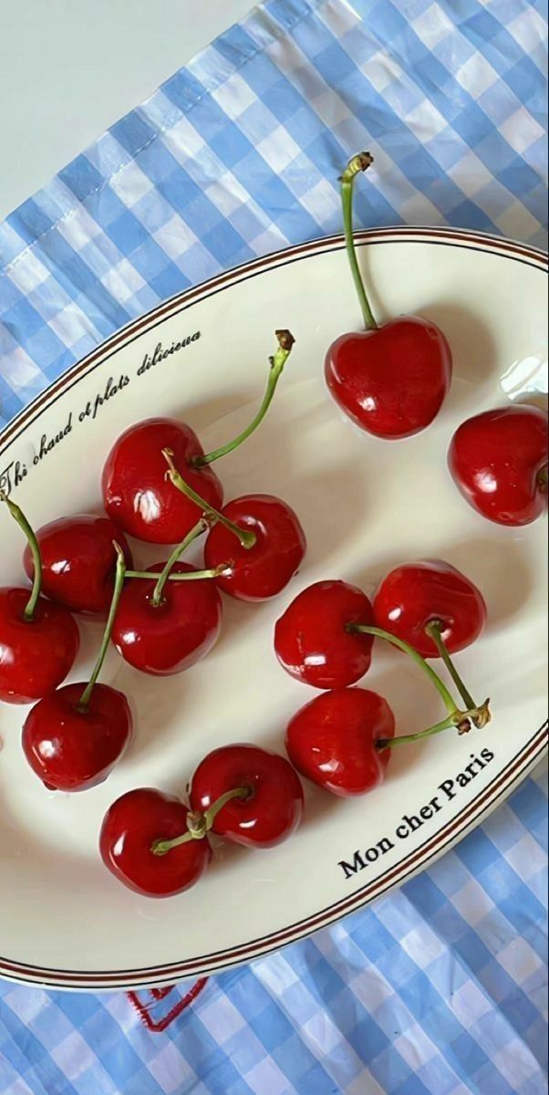 cherries on a plate sitting on a blue and white checkered tablecloth