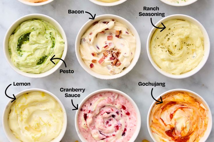 six different types of dips in white bowls on a marble counter top, labeled with their names