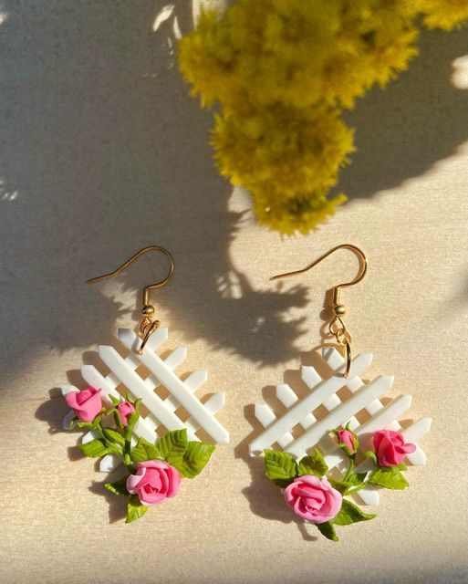 white picket fence earrings with pink roses and green leaves on them next to yellow flowers