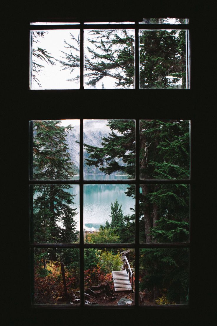 an open window looking out onto a lake and forest with a bench in the foreground