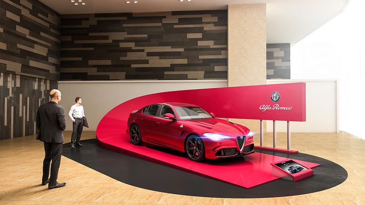 two men standing next to a red car on display