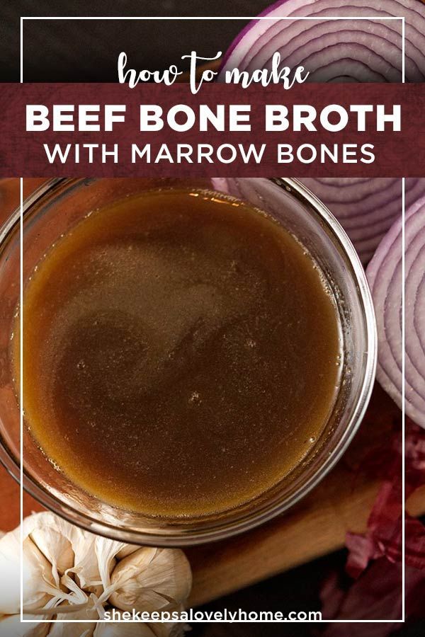 a bowl filled with beef bone broth next to onions and garlic on a cutting board