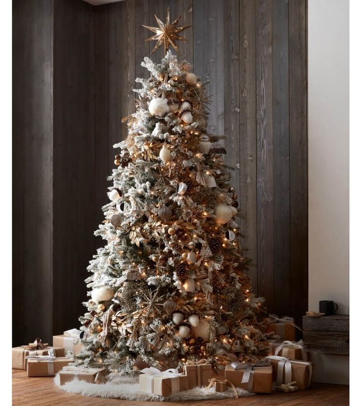 a christmas tree with presents under it in front of a fire place and wooden wall