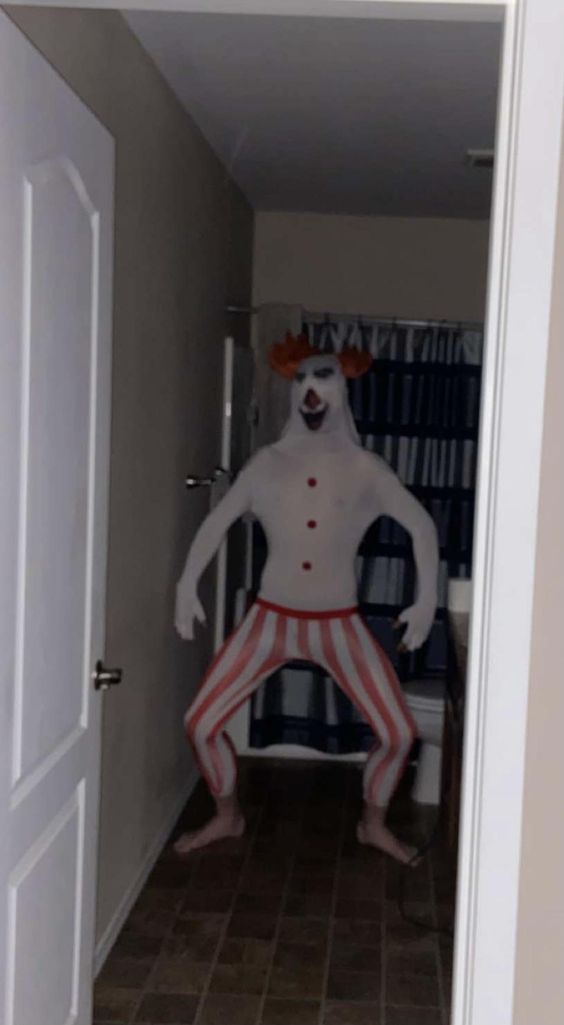 a man dressed as a clown is standing in the hallway with his legs spread out