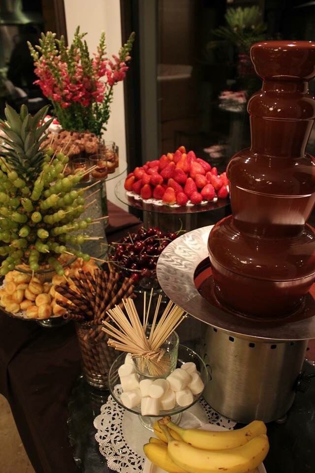 chocolate fountain surrounded by fruit and flowers on a table