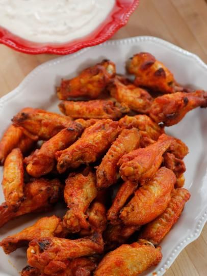 some chicken wings on a white plate with sauce in the bowl behind it and a red glass dish