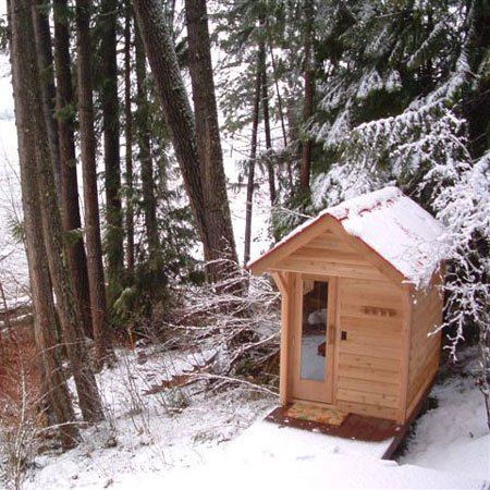 a small wooden outhouse in the woods with snow on the ground and trees around it