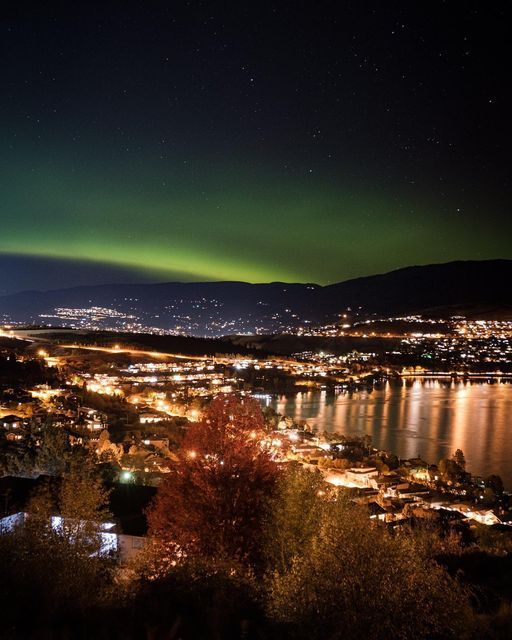 the northern lights shine brightly over a city at night, with mountains in the background