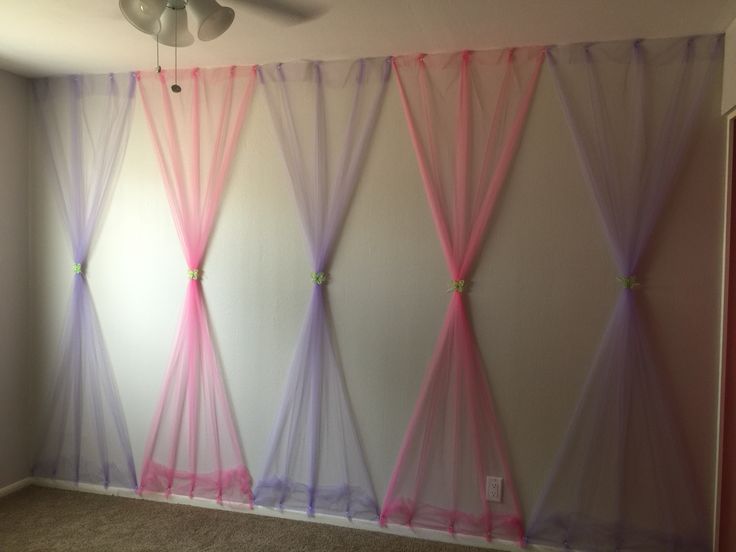 an empty room with pink, purple and blue sheer curtains on the wall in front of a ceiling fan