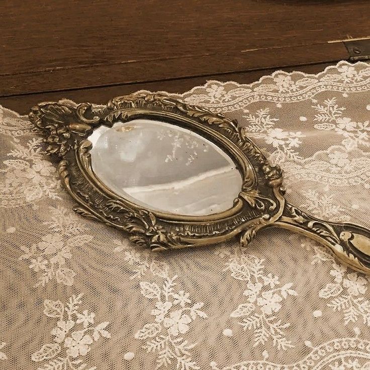 a mirror sitting on top of a table next to a lace covered table cloth and wooden drawer