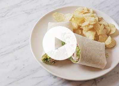 a white plate topped with chips and a wrap filled with veggies next to potato chips