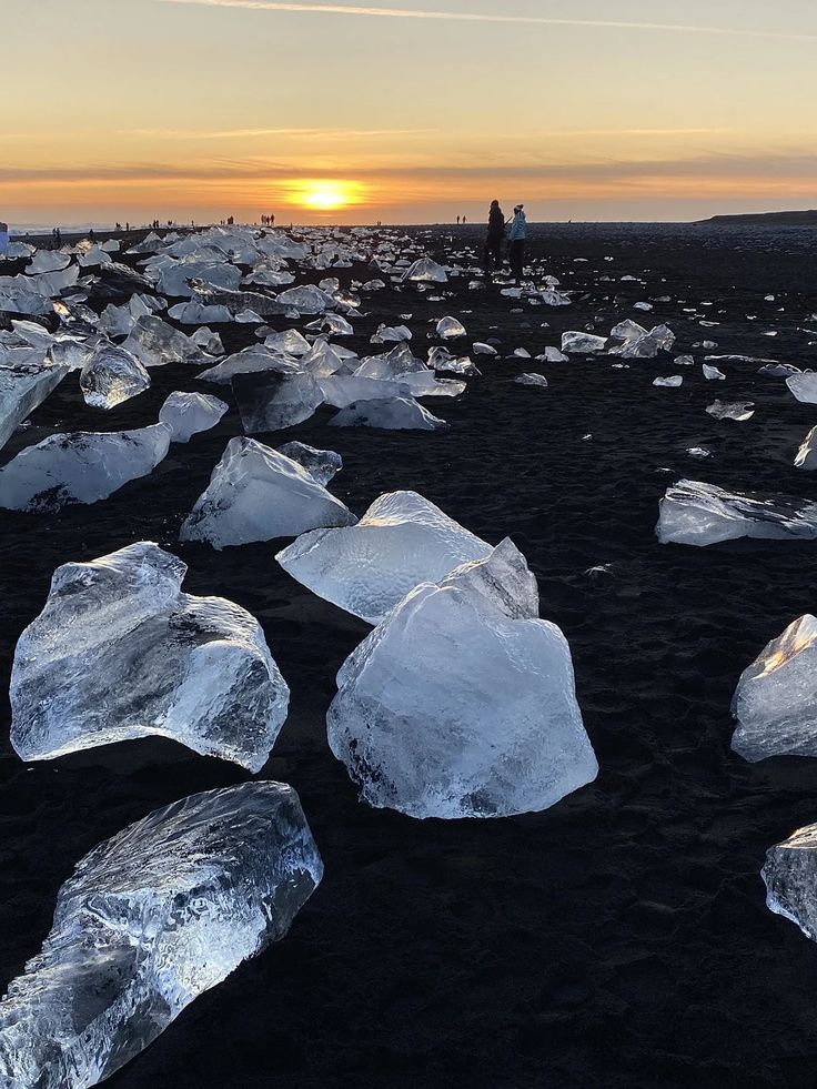 the sun is setting over some icebergs on the black sand at low tide