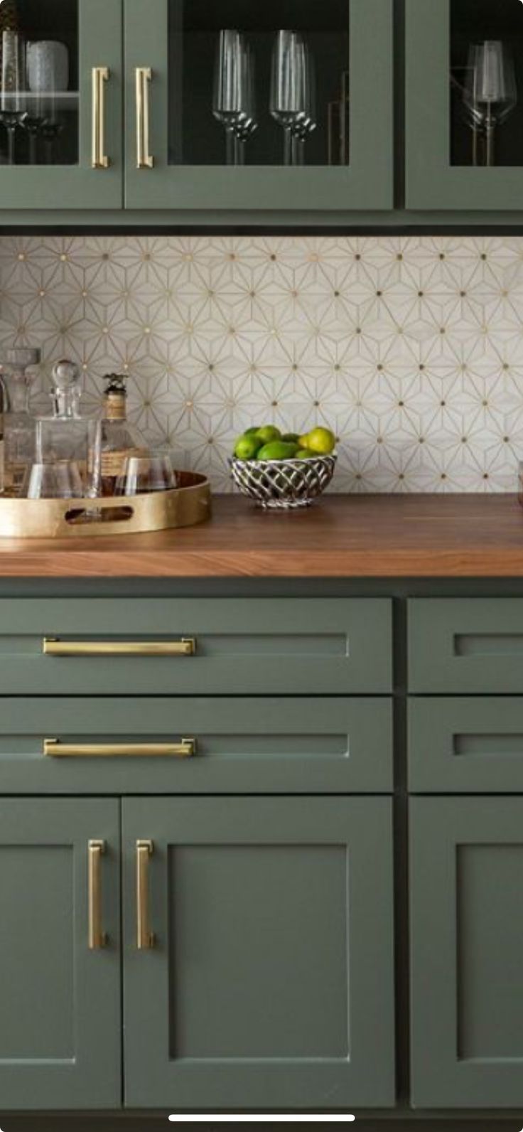 a kitchen with green cabinets and white tile backsplash, gold handles and brass pulls