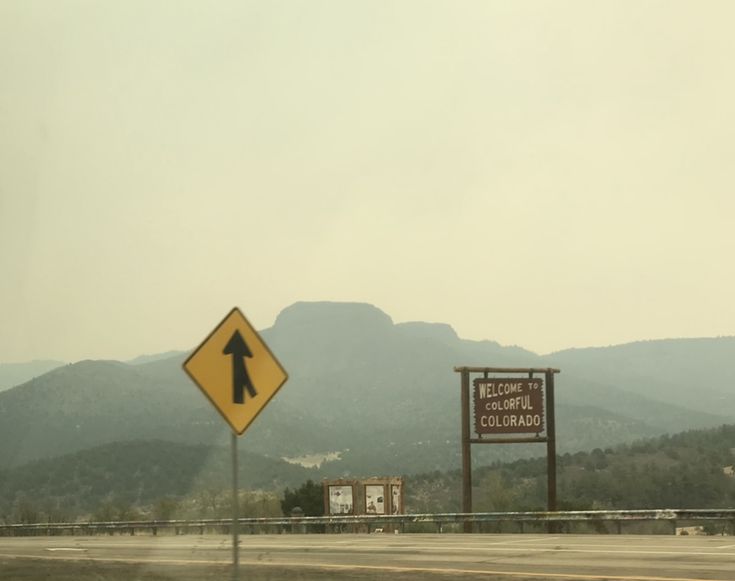 a road sign with mountains in the background and foggy sky above it on a cloudy day