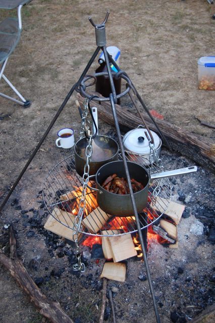 an outdoor cooking area with pots and pans on the fire, next to a campfire