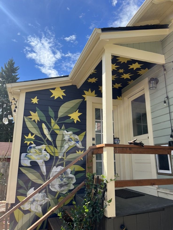 a house painted with flowers and stars on the side, under a blue sky filled with wispy clouds