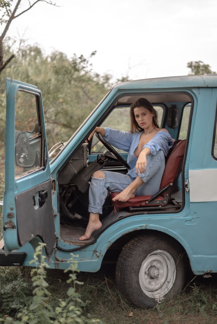 a woman sitting in the driver's seat of an old blue truck with her foot on the steering wheel