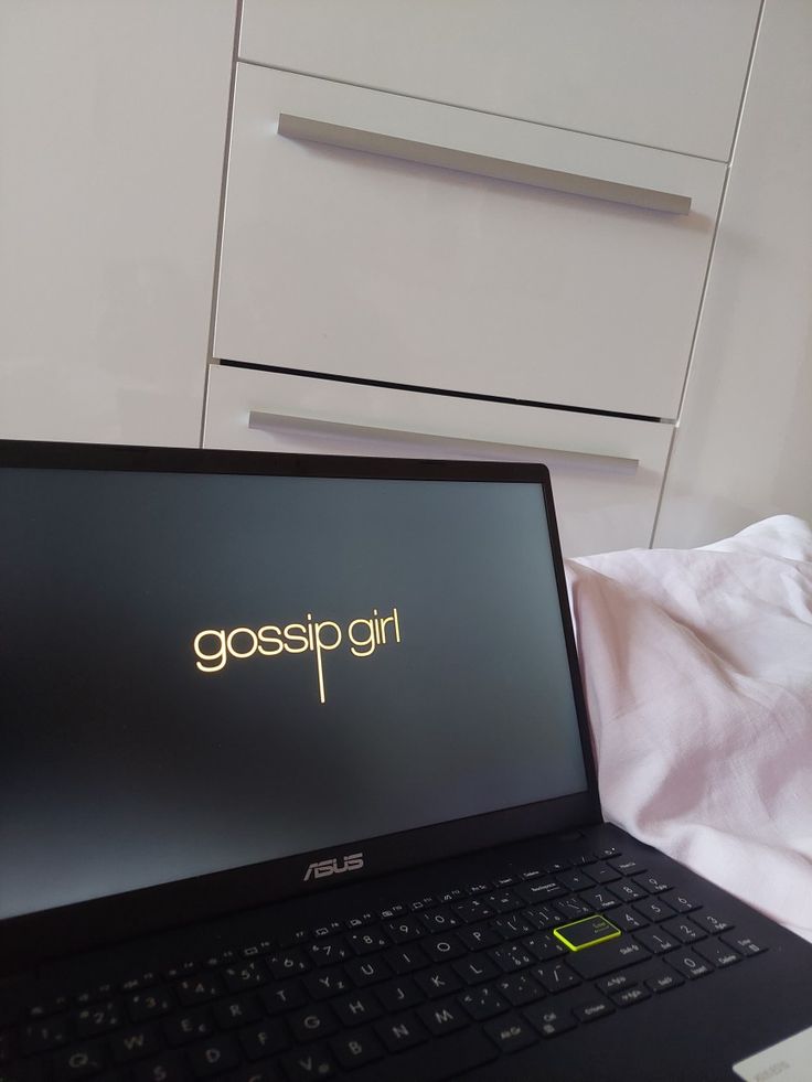 an open laptop computer sitting on top of a bed next to a white dresser and drawers