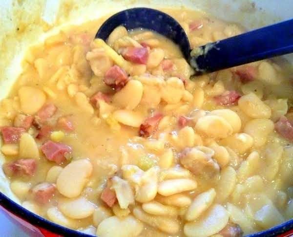 a pot filled with beans and ham cooking on top of a stove next to a blue spatula