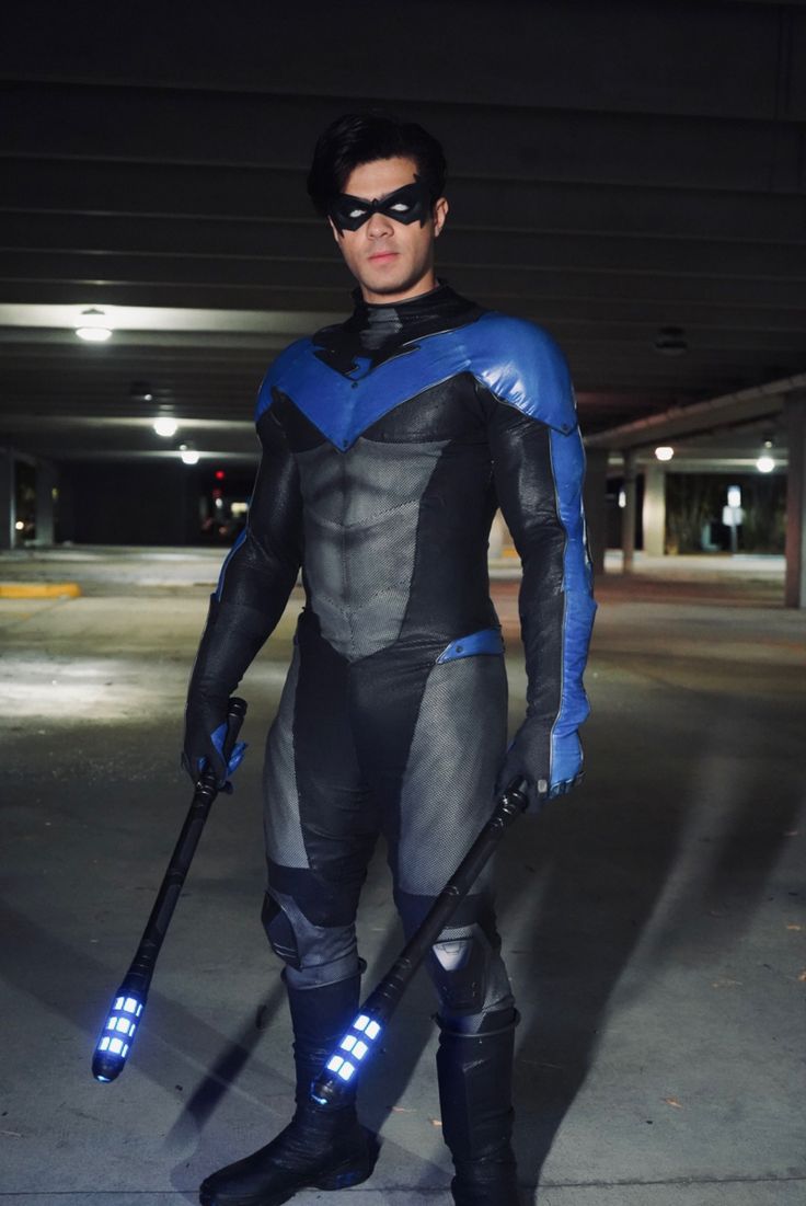 a man dressed as batman standing in an empty parking lot at night with his bat