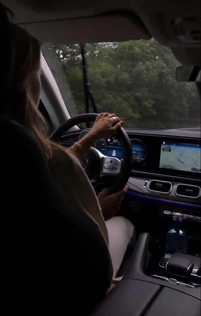 a woman driving a car on a road with trees in the backgrouund