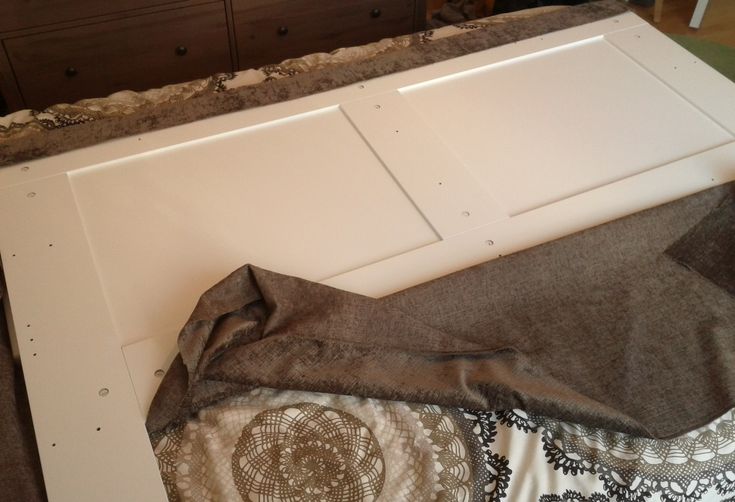 an unfinished bed frame is laying on top of the floor and covered with fabric, next to a dresser