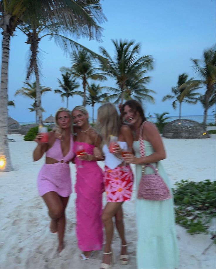 four beautiful women standing next to each other on a beach with palm trees in the background