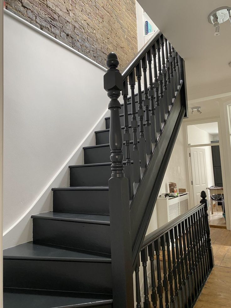 there is a black stair case next to the brick wall in this house with white walls