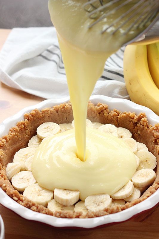 a banana pie is being drizzled with white icing on a wooden table