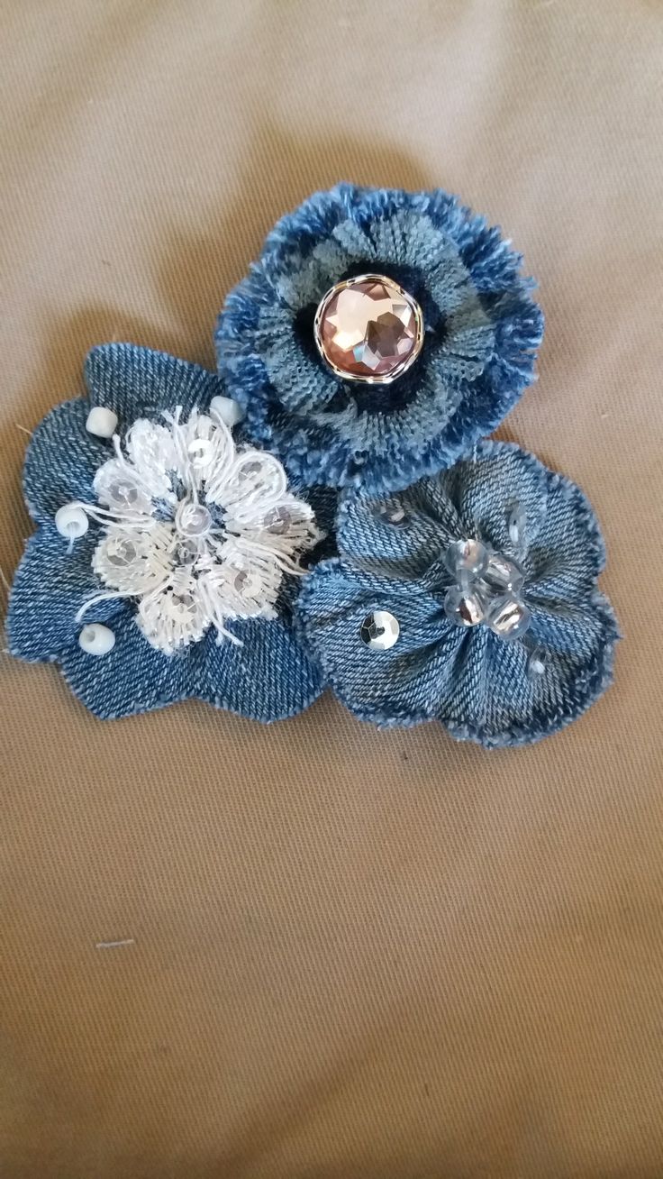 three blue flowers are sitting on a tan cloth covered tablecloth with beads and sequins