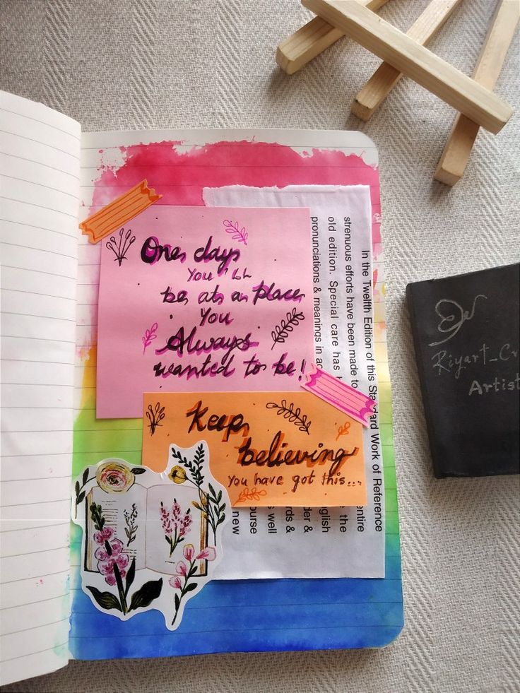 an open notebook with colorful papers and writing on the pages next to a small black book