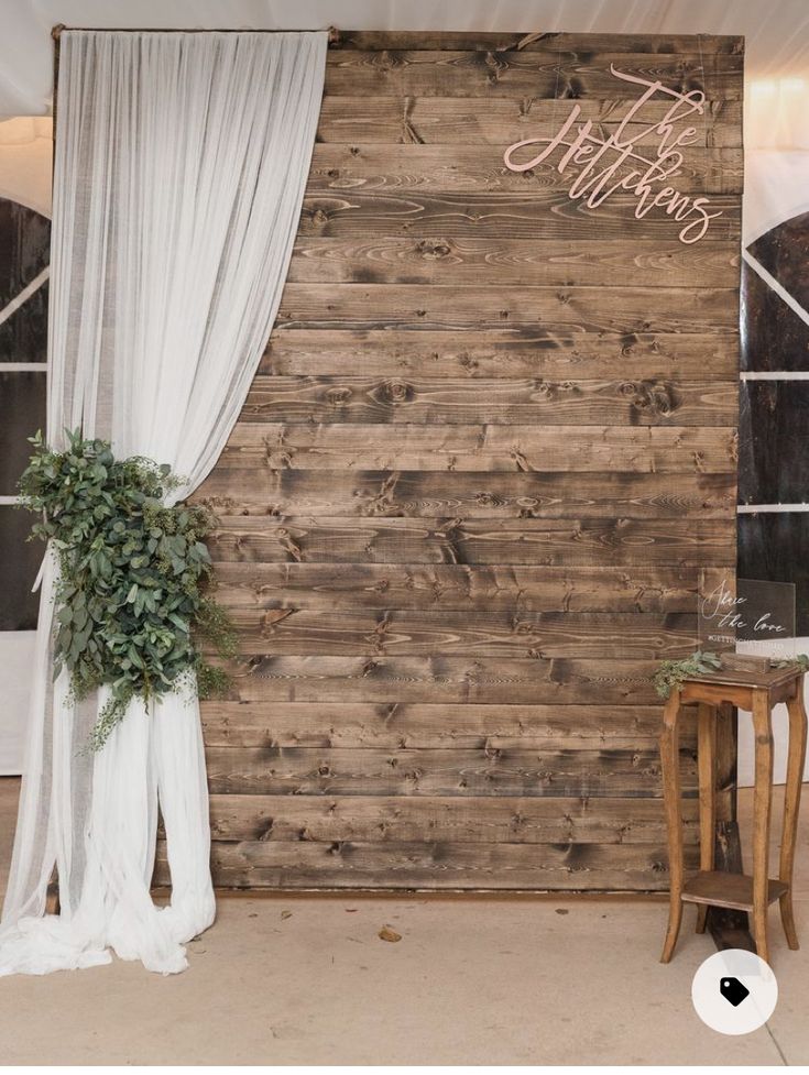 a wooden wall with white drapes and greenery