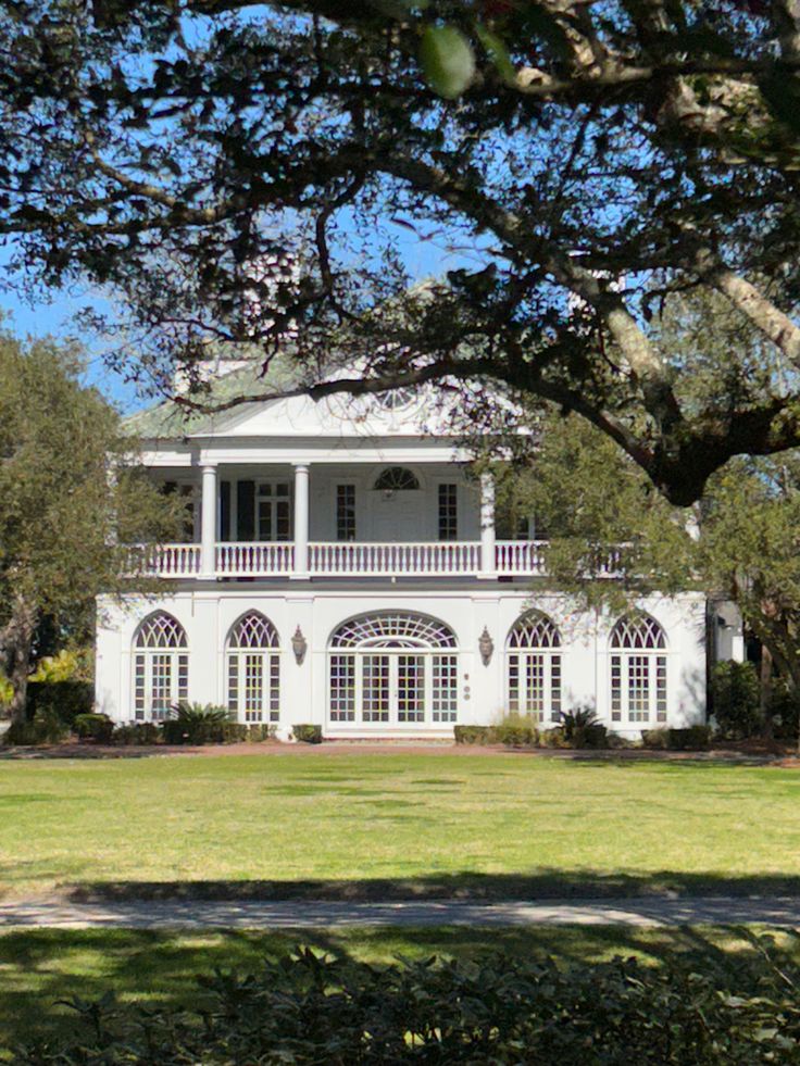 a large white house sitting in the middle of a lush green field next to trees