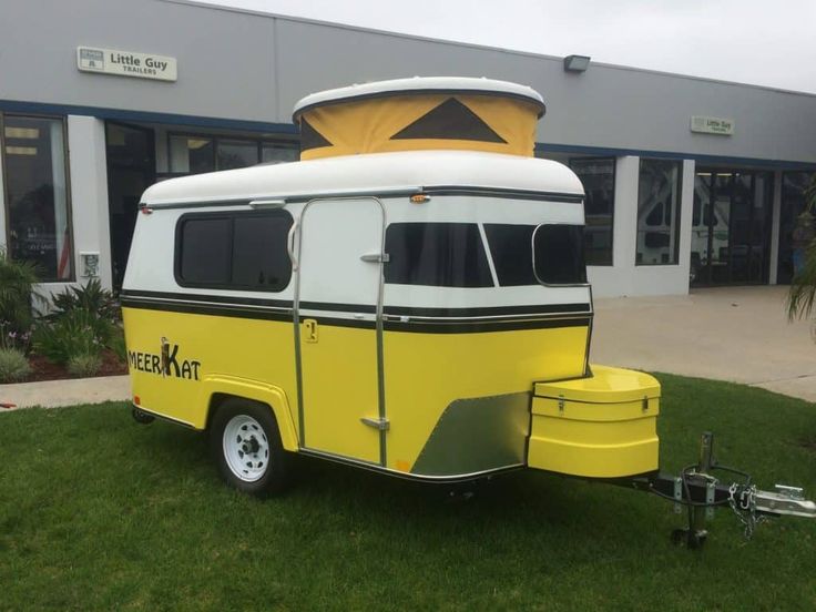 a yellow and white camper trailer parked in front of a building on the grass